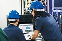 Two engineers reviewing data on a monitor in an industrial setting, representing Windchill PLM platform